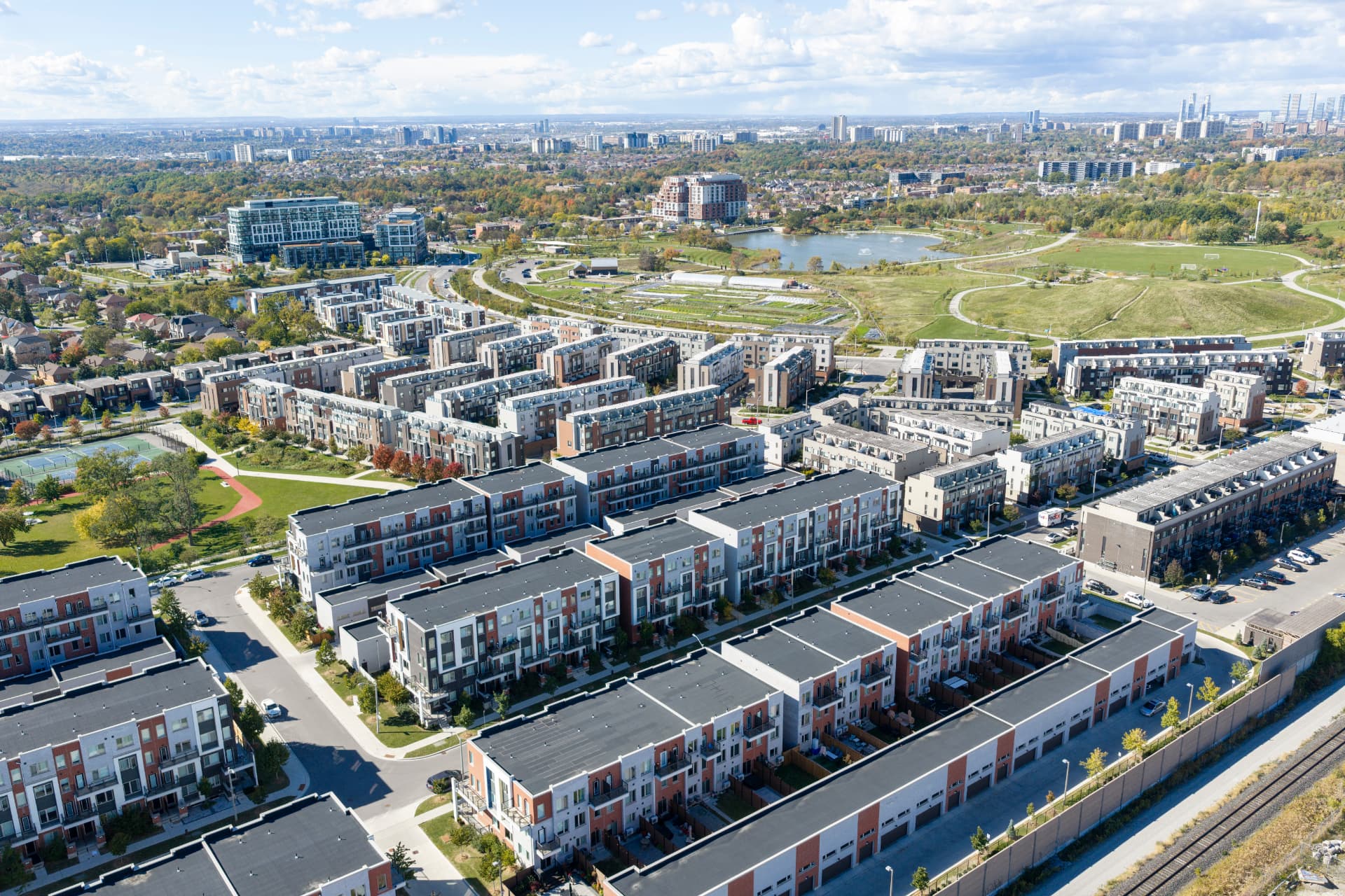 Aerial view of the Downsview Park neighbourhood with townhomes, the park's lake and green space, and the Toronto skyline