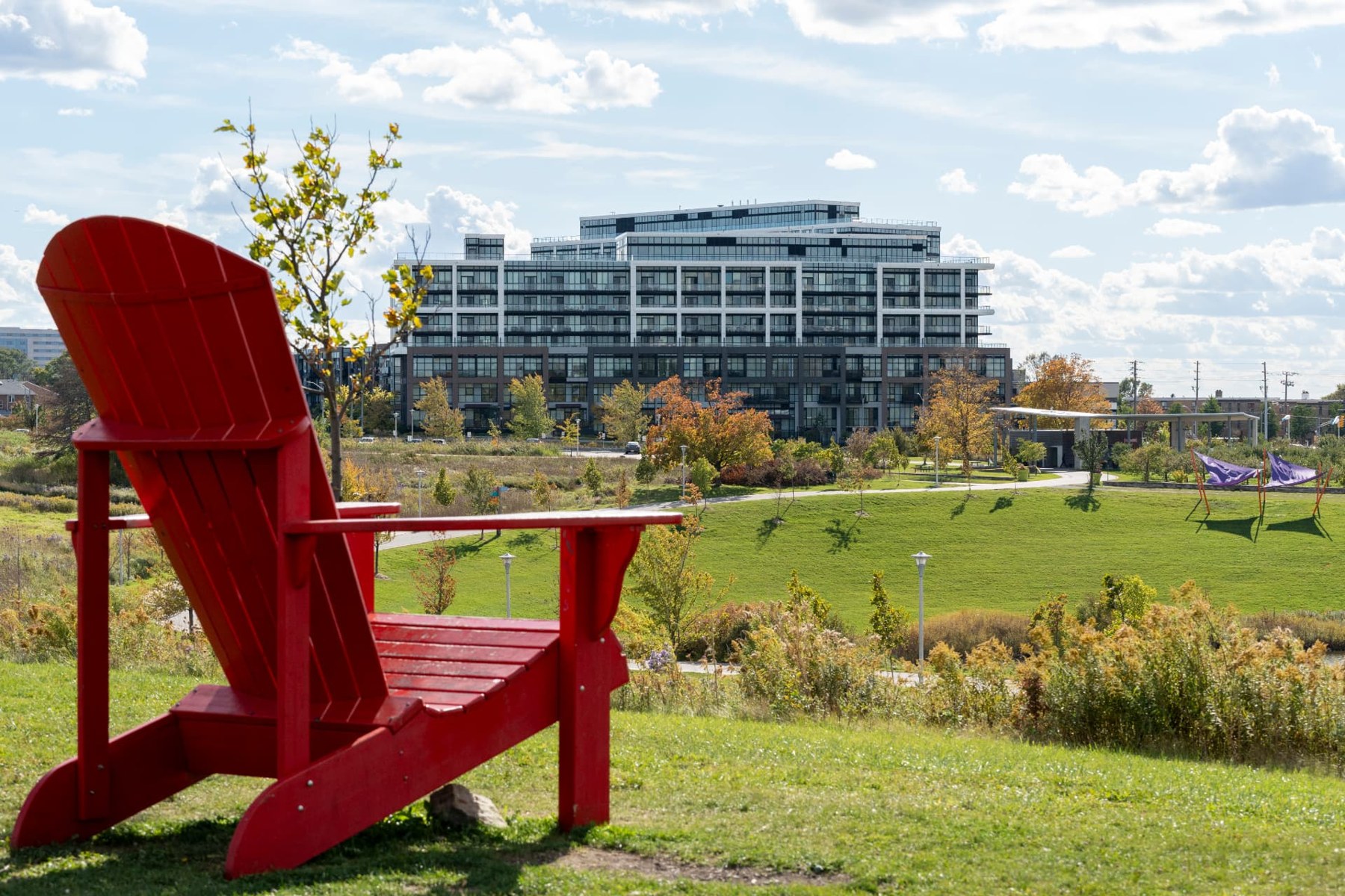 A red Muskoka chair overlooking Downsview Park with a residential building beyond